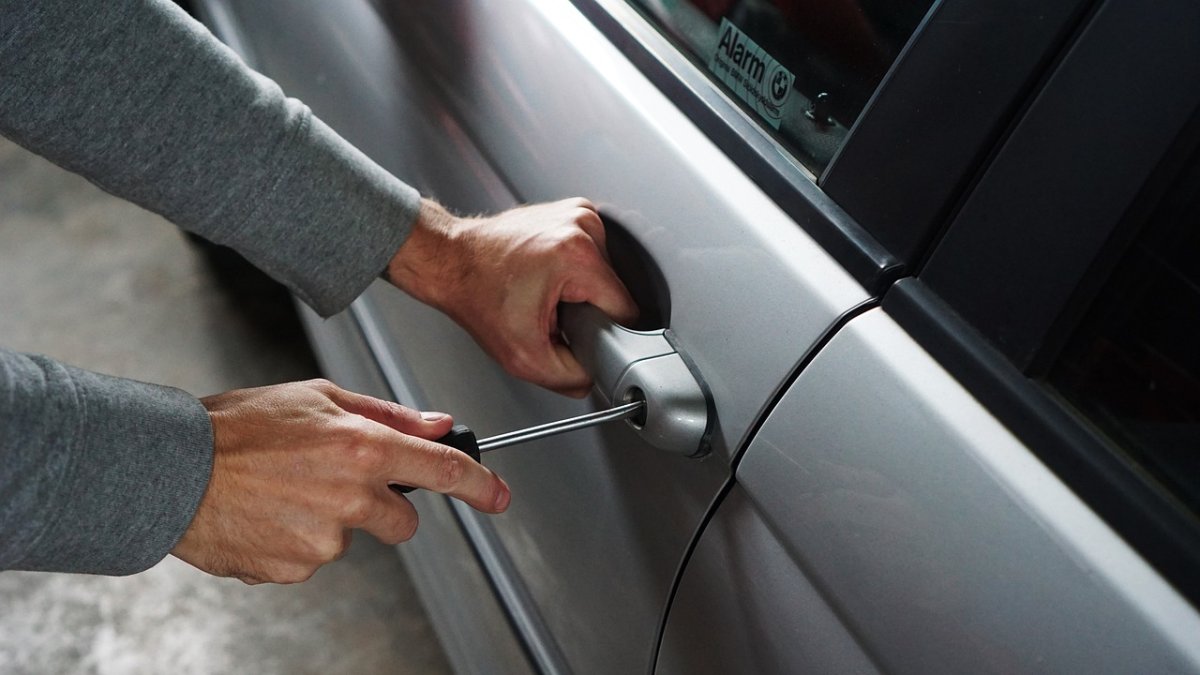 Imagen de un ladrón intentando forzar la puerta de un coche con un destornillador.
