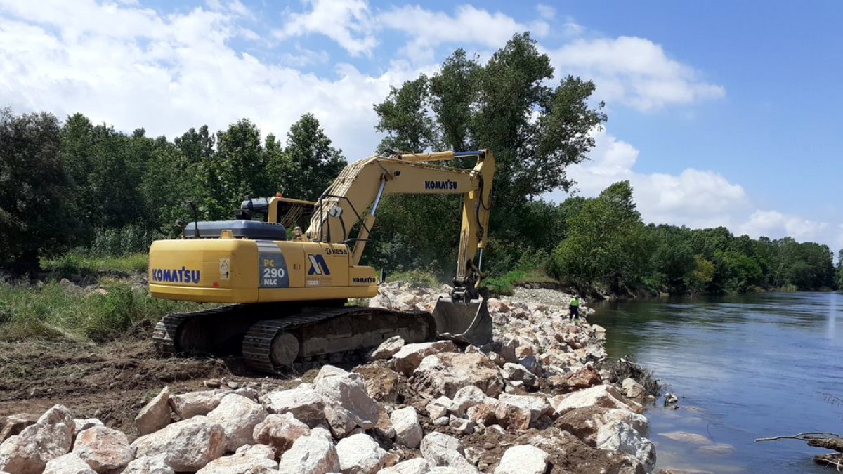 Una retroexcavadora trabaja en la construcción de un muro de protección delante de avenidas de agua