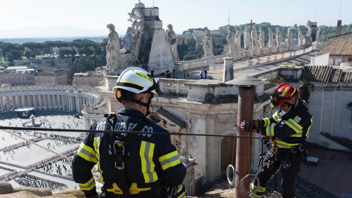 Dos operarios colocan la chimenea sobre la Capilla Sixtina que anunciará la elección de un nuevo Papa