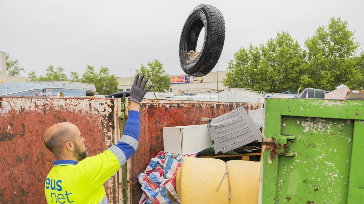 Un trabajador de Reus Net depositando basura en un contenedor lleno de desperdicios abandonados en la vía pública.