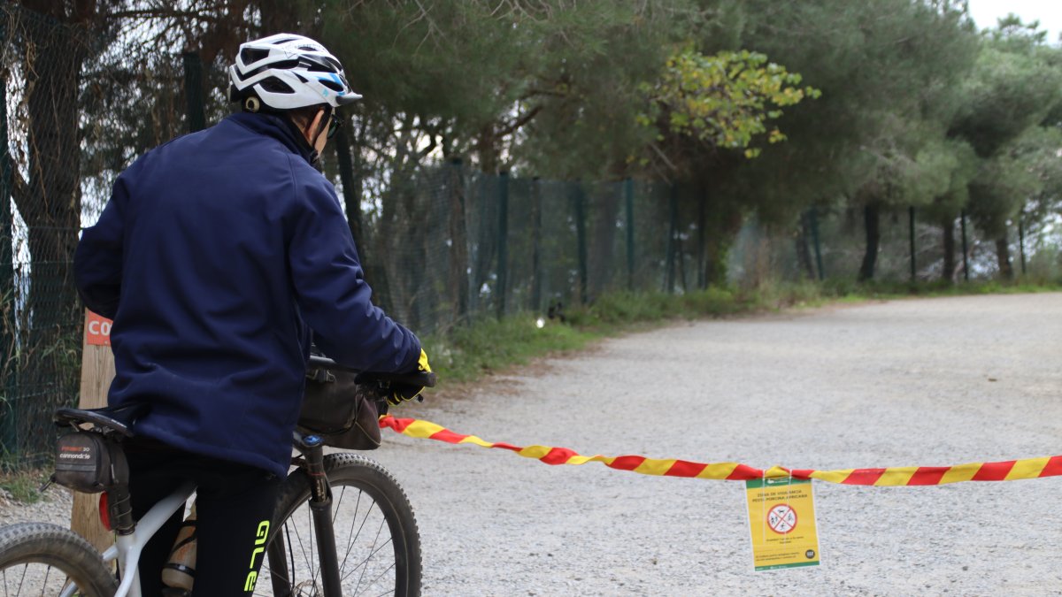 Un ciclista llegint el cartell que indica la prohibició d'accedir a Collserola a la carretera de les Aigües de Barcelona.