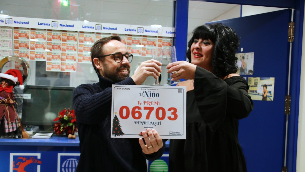 Dos trabajadores de la administración Doña Pilar de Salou brindando con cava y mostrando el cartel del primer premio del Sorteo del Niño.