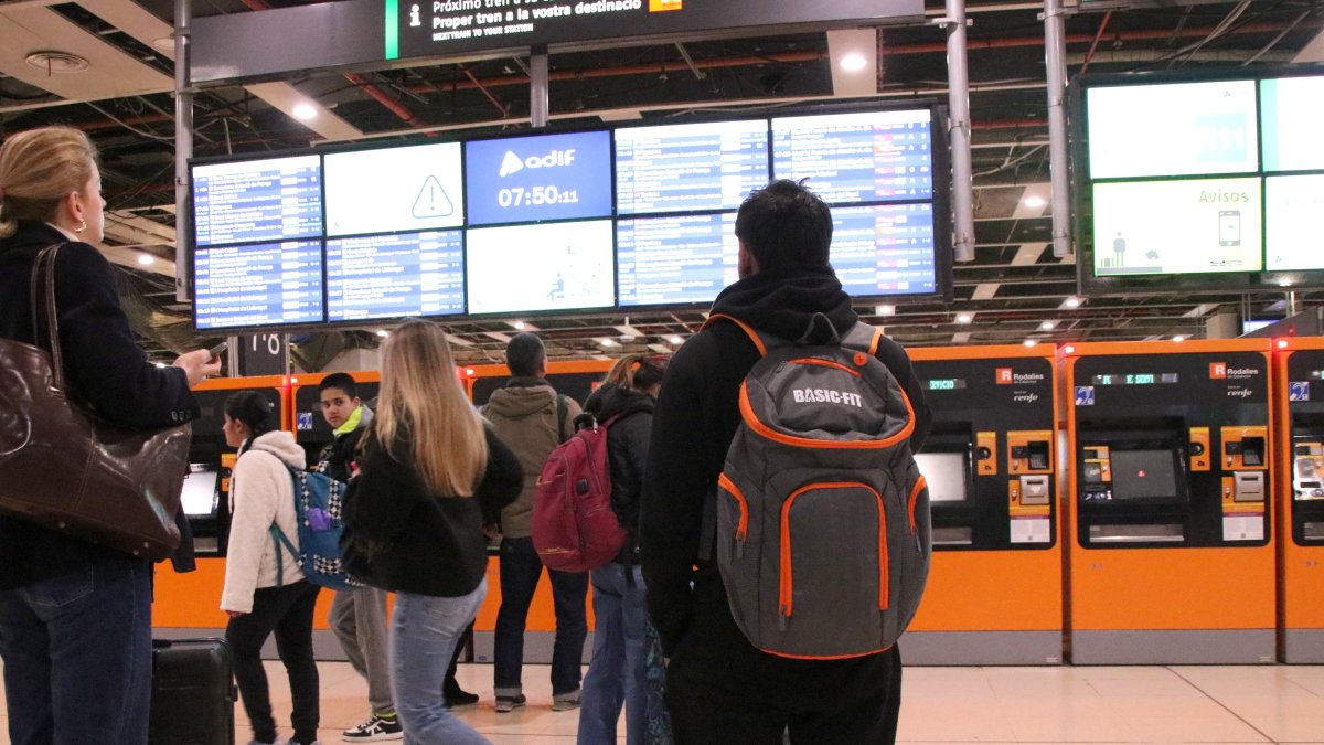 Personas mirando los paneles informativos de los horarios de Rodalies en la estación de Sants.