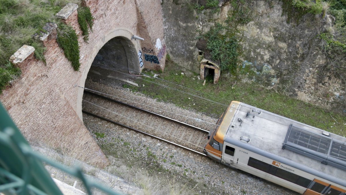 Vista desde un talud de un tren de la R1 entrando en un túnel en un tramo donde hay circuación por vía única