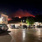 Cotxes aparcats a la plaça major de Paüls amb el foc cremant al fons.
