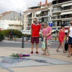 Plano abierto de varias personas paradas delante del Memorial per la Pau de Cambrils, con un ramo de flores.