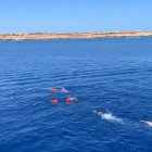 Quatre rescatats per l'Open Arms es llencen a l'aigua i són perseguits per socorristes, amb la costa de Lampedusa al fons.