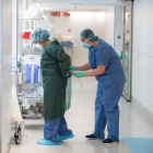 Una profesional sanitaria ata a una compañera una bata antes de atender a un paciente con covid-19, en uno de los bloques quirúrgicos del Hospital Clínico de Barcelona habilitado como UCI en la pandemia de coronavirus.