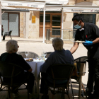 Dos clients d'esquenes i d'un cambrer servint els plats en una terrassa de la plaça de la Font