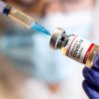 Una mujer tiene una jeringa médica y una botella pequeña con la etiqueta 'Vacuna contra el coronavirus covid-19'.