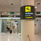Un senyal de la zona d'Arribades amb un passatger arrossegant una maleta de fons a l'Aeroport del Prat.