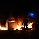 Silueta de un agente de los antidisturbios de los Mossos d'Esquadra delante de varios contenedores quemados durante las protestas.