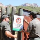 Dos Agents Rurals col·loquen un cartell informatiu a l'accés al Parc Natural de la Serra de Montsant.