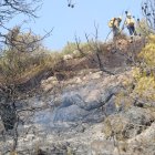 Imatge d'arxiu de l'incendi que mostra una branca encara fumeja mentre dos bombers remullen la zona afectada per l'incendi de la Figurera