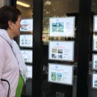 Una dona revisa les ofertes de pisos a la venda fora d'una immobiliària.