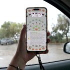 Un telèfon mòbil, amb l'alerta de Protecció Civil, i un carrer ple d'aigua de pluja al fons, a Amposta